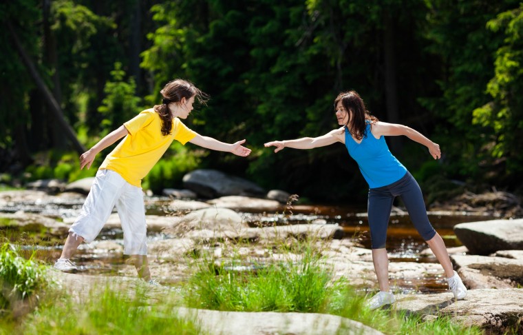 A young girl and a young woman helping each other across the stream